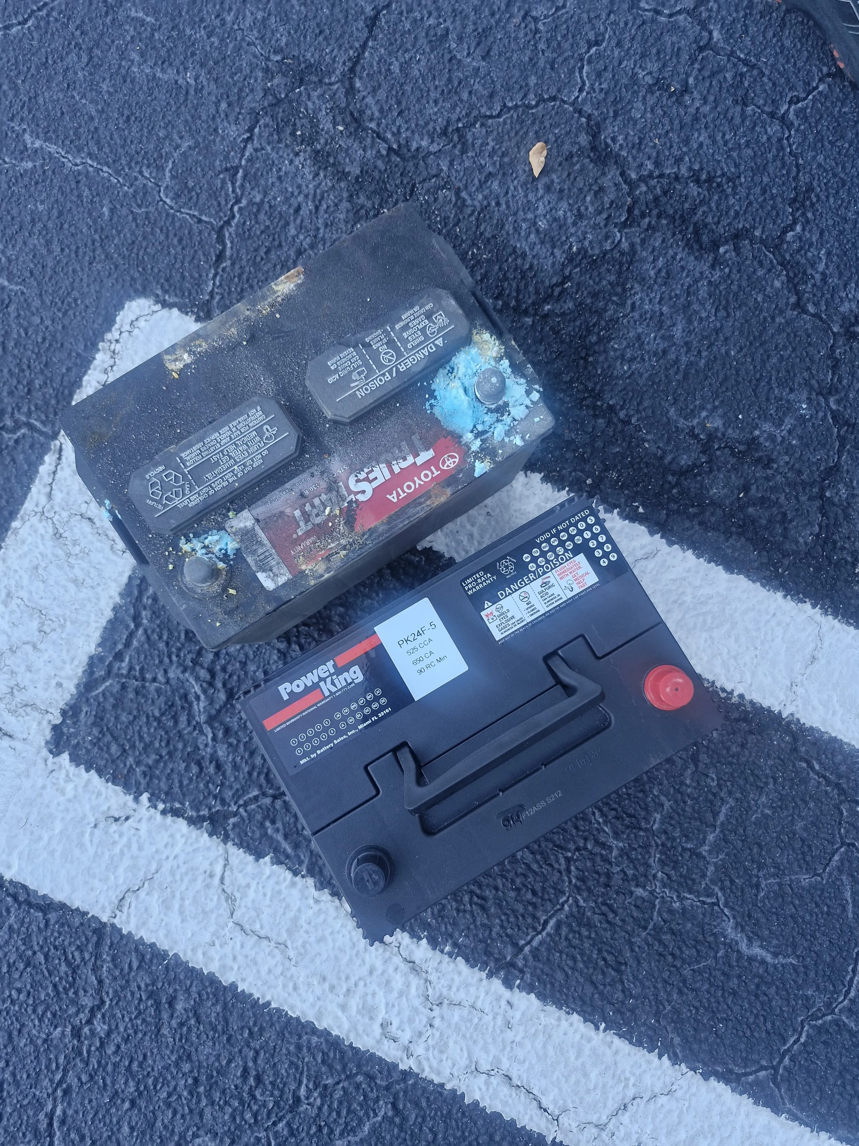 Corroded Toyota battery beside a clean Power King battery on the pavement