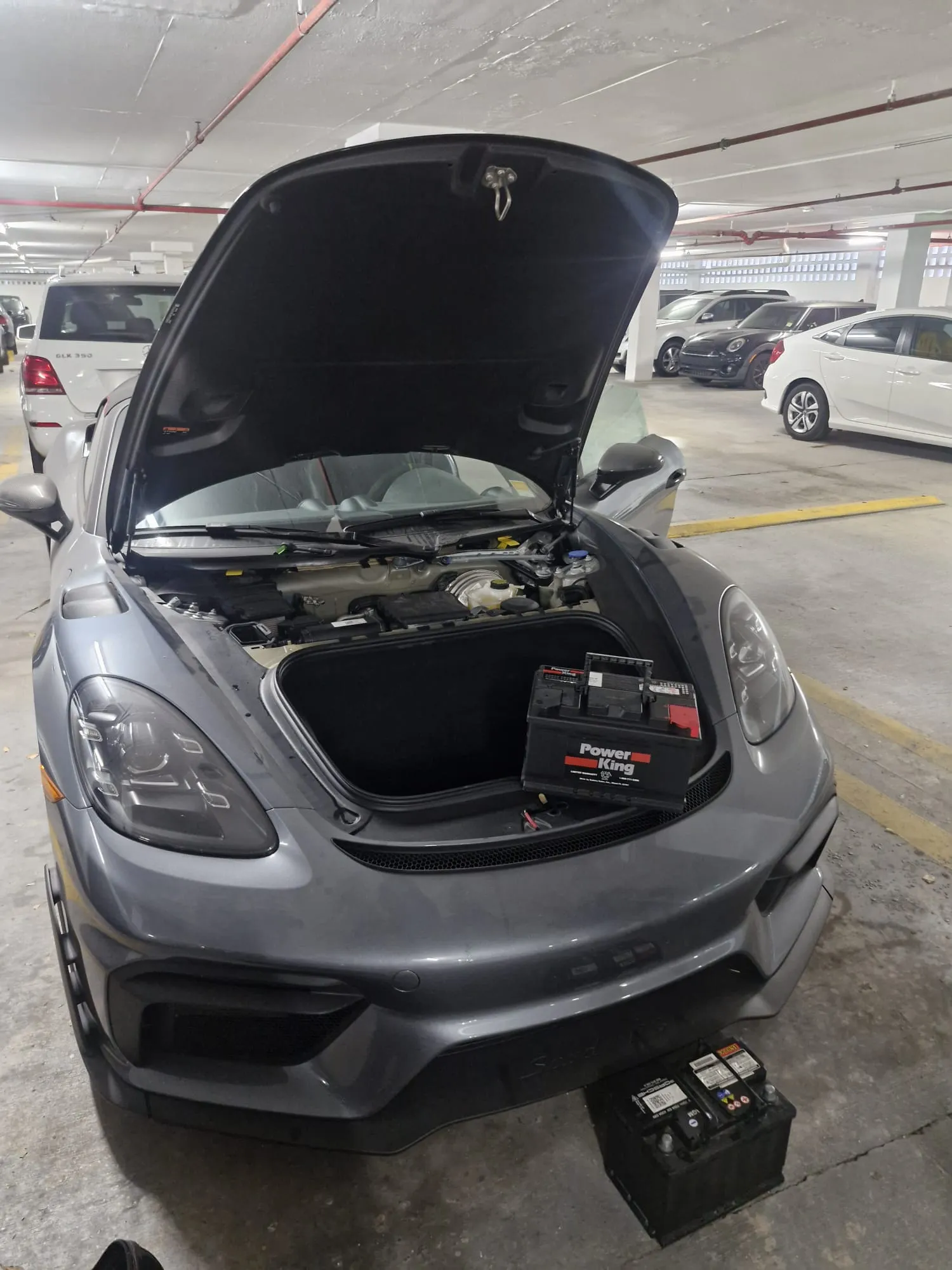 Porsche with its front hood open and battery service equipment on location